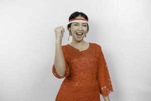 A young Asian woman with a happy successful expression wearing red kebaya and headband isolated by white background. Indonesia's independence day concept. photo