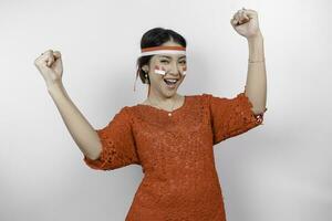 A young Asian woman with a happy successful expression wearing red kebaya and headband isolated by white background. Indonesia's independence day concept. photo