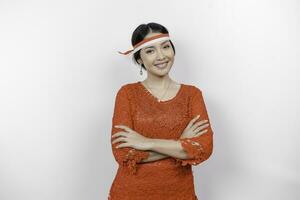 A confident Indonesian woman folding her arms and wearing red kebaya and Indonesia's flag headband to celebrate Indonesia Independence Day. Isolated by white background. photo