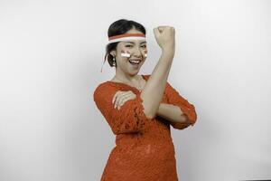 emocionado asiático mujer vistiendo un rojo kebaya y venda demostración fuerte gesto por levantamiento su brazos y músculos sonriente con orgullo de indonesia independencia día concepto. foto