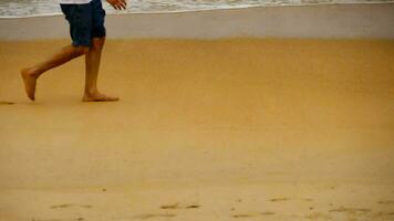 Tourist man feet walking on the tropical beach along sea water waves. Slow motion beach walking video