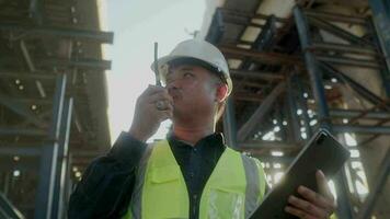 A engineer supervises road construction, commands with Walkie-Talkie radio communication helmet working on tollway construction site. video