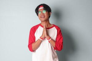 Portrait of attractive Asian man in t-shirt with red and white ribbon on head, pulling hands towards camera, inviting someone to come inside, welcoming gesture. Isolated image on gray background photo