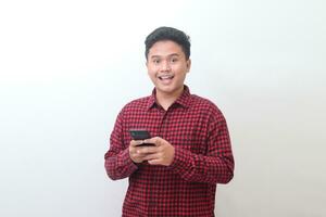 Portrait of attractive Asian man in casual plaid shirt holding mobile phone and looking at camera. Isolated image on white background photo