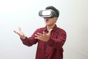 Portrait of Asian man in red plaid shirt using Virtual Reality VR glasses and protecting himself by spreading his arms from something big falling from above. Isolated image on white background photo