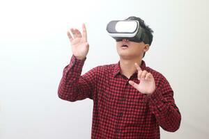 Portrait of Asian man in red plaid shirt using Virtual Reality VR glasses and protecting himself by spreading his arms from something big falling from above. Isolated image on white background photo