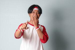 retrato de atractivo asiático hombre en camiseta con rojo y blanco cinta en cabeza, señalando adelante a el cámara. aislado imagen en gris antecedentes foto