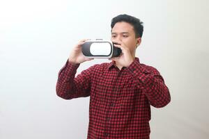 Portrait of Asian man in red plaid shirt getting ready and using Virtual Reality VR. Isolated image with copy space on white background photo