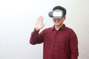 Portrait of Asian man in red plaid shirt using Virtual Reality VR glasses and greet his friend inside the game with opened palm. Isolated image on white background photo