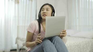 Beautiful woman at home sitting on the sofa while using laptop and headphone. video