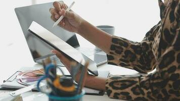 Caucasian female fashion designer works in studio by idea drawing sketches with digital tablet and colorful fabric for a dress design collection, choose clothing colors for tailoring and designing video