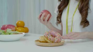 eetpatroon en op dieet zijn. schoonheid slank vrouw lichaam verwarren donut. vrouw in oefening kleren behaalt gewicht verlies doel voor gezond leven, gek over dunheid, dun taille, voedingsdeskundige. video