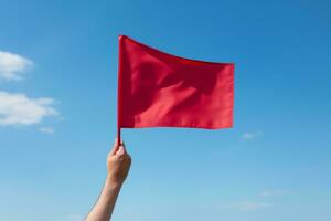 Hand holding red flag against blue sky photo