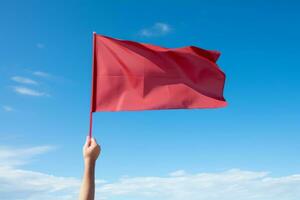 Hand holding red flag against blue sky photo