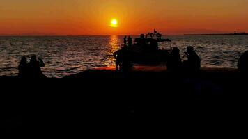 silhouetten van boot en mensen ontspannende en visvangst in avond weinig momenten voordat zonsondergang met zon en wolken reflectie zee water. video