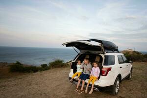 Three kids sitting in a car trunk on the beach by the sea. Cape Emine, Black sea coast, Bulgaria. photo