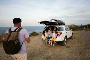 Father and kids sitting in car trunk on seashore at sunset. Cape Emine, Black sea coast, Bulgaria. photo