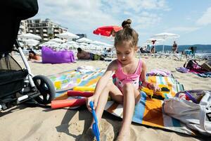 pequeño niña sentar en cobija y jugando en el playa. foto