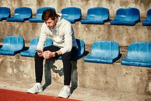 Man in sportswear resting at stadium seat and use smartphone photo