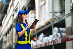 Worker in blue dress inspects, handles goods in a warehouse. Female worker using tablet working in logistic export-import industry. photo