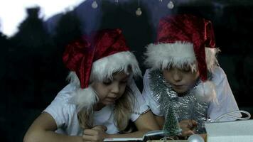 dois crianças dentro santa chapéus estão sentado às uma mesa video