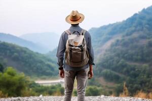 Back view of young man with backpack and hat standing on top of the mountain photo