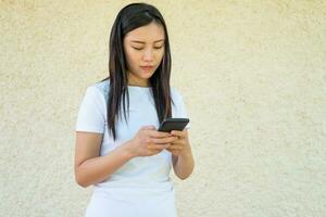 chino mujer en un blanco camiseta mirando a su móvil foto