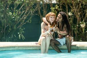 afroamericano hombre y blanco mujer tostado con cerveza botellas en el borde de un piscina. foto