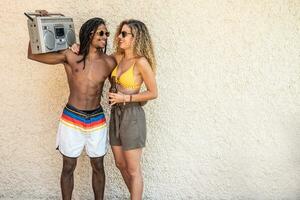 black man with a stereo in his hands hugging a white woman in a bathing suit photo