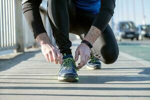 Young man tying laces of running shoes before training,closeup on shoe. photo