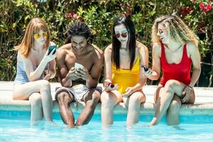 people of different races in swimsuits at the edge of a pool using mobile phones photo