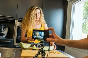 mujer grabación con un cámara me gusta un melón cortador en un cocina foto