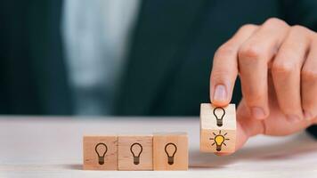 Leader choosing the best new idea with light bulb icon on wooden blocks. Explore creative design, solutions, strategy reviews. Inspiring innovation and teamwork. photo