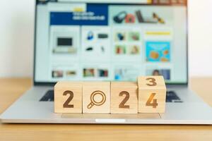 2024 block with magnifying glass icon against laptop background. Hiring, recruitment, job, jobless SEO, Search Engine Optimization and New Year concepts photo