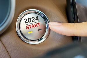 Finger press a car ignition button with 2024 START text inside  automobile. New Year New You, forecast, resolution, motivation, change, goal, vision, innovation and planning concept photo