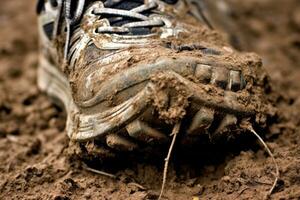 Close - up photo of a trail runner's worn - out trail running shoes covered in mud and dirt. Generative AI