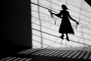 A witch's silhouette being cast on a wall, with the prominent shadow of a broomstick suggesting flight.  Generative AI photo