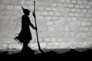 A witch's silhouette being cast on a wall, with the prominent shadow of a broomstick suggesting flight.  Generative AI photo