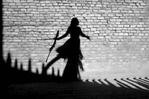 A witch's silhouette being cast on a wall, with the prominent shadow of a broomstick suggesting flight.  Generative AI photo