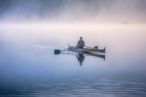 On a quiet, foggy morning, a fisherman casts his net on a serene lake. photo
