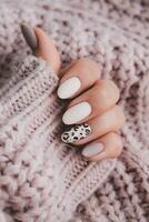 A woman's hand with a beautiful manicure holds a beige fabric. Autumn trend, beige color polishing with leopard pattern on nails with gel polish, shellac. photo