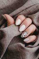 A woman's hand with a beautiful manicure holds a beige fabric. Autumn trend, beige color polishing with leopard pattern on nails with gel polish, shellac. photo