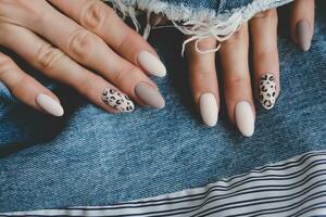 Beautiful female hands with manicure on the background of denim. Stylish nail design. Autumn manicure with beige color and leopard pattern on the nails. photo