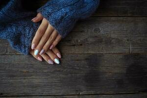 Women is hands with a beautiful manicure, in a knitted sweater on a wooden background in. Autumn trend, polish beige and white polka dots on nails with gel polish, shellac. Close up. photo