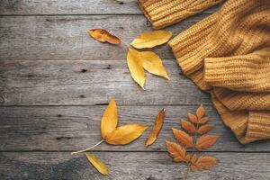 Autumn leaves and knitted sweater on old wooden background . Copy space photo