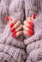 Women's hands with a beautiful matte oval manicure in a warm pink knitted sweater. Winter trend, cover red nails with gel polish, shellac. photo