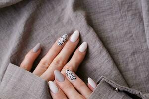 A woman's hand with a beautiful manicure holds a beige fabric. Autumn trend, beige color polishing with leopard pattern on nails with gel polish, shellac. photo