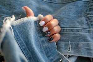 hermosa hembra manos con manicura en el antecedentes de mezclilla. elegante uña diseño. manicura con negro y blanco cebra rayas en el clavos. foto