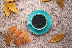 A cup of coffee on a knitted pink sweater. Tea and yellow leaves on an autumn background. photo