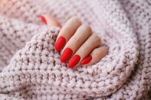 De las mujeres manos con un hermosa mate oval manicura en un calentar rosado de punto suéter. invierno tendencia, cubrir rojo uñas con gel polaco, goma laca. foto